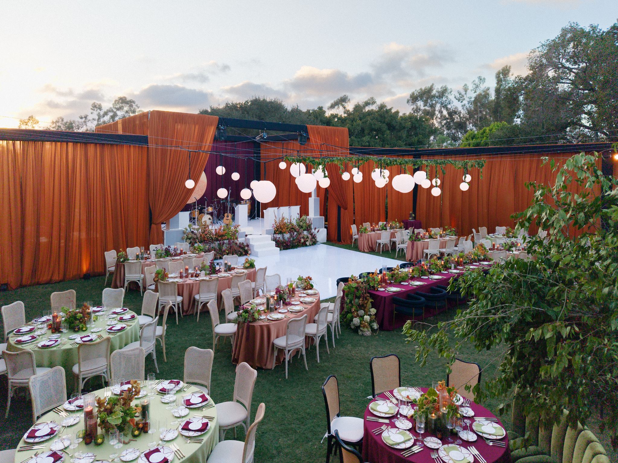 Black tie wedding reception at Rancho Valencia at dusk, with a draped structure, hanging lanterns and dressed tables on the Croquet Lawn