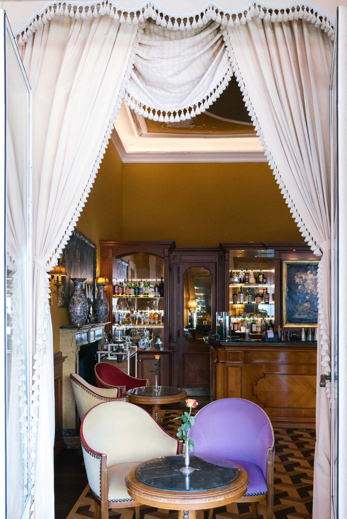 Historic bar at the Grand Hotel Tremezzo framed by white draped curtains, with velvet armchairs and carved wood interior