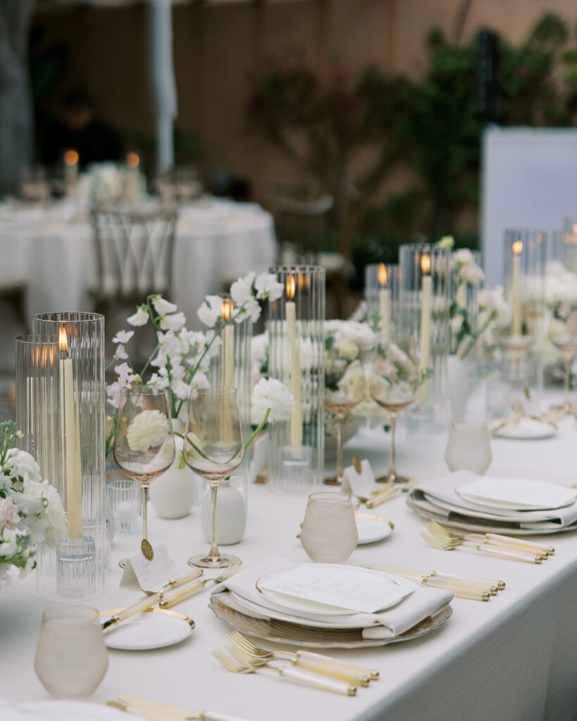 Candlelit long reception table with white florals and gold flatware, timed through a wedding production schedule