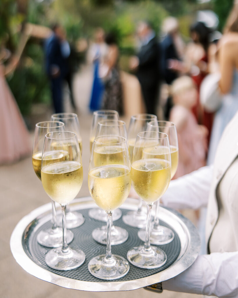 Tray of champagne flutes served at a garden cocktail hour, timed in a wedding production schedule