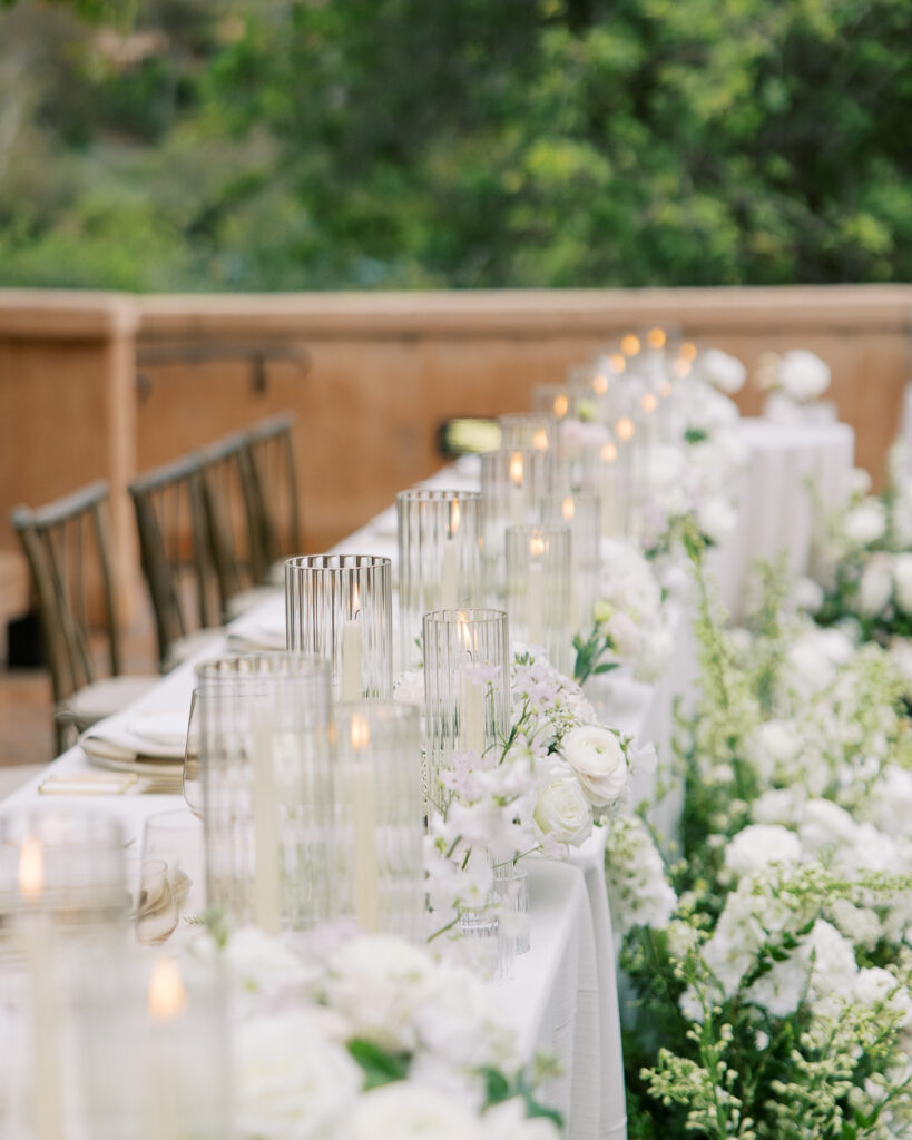 Long reception table with a white floral runner and candles, set from a wedding production schedule